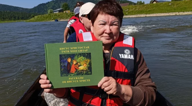 Lidé národa Shoria jedou po řece na lodi a vezou si knihy bible přeložené do svého jazyka